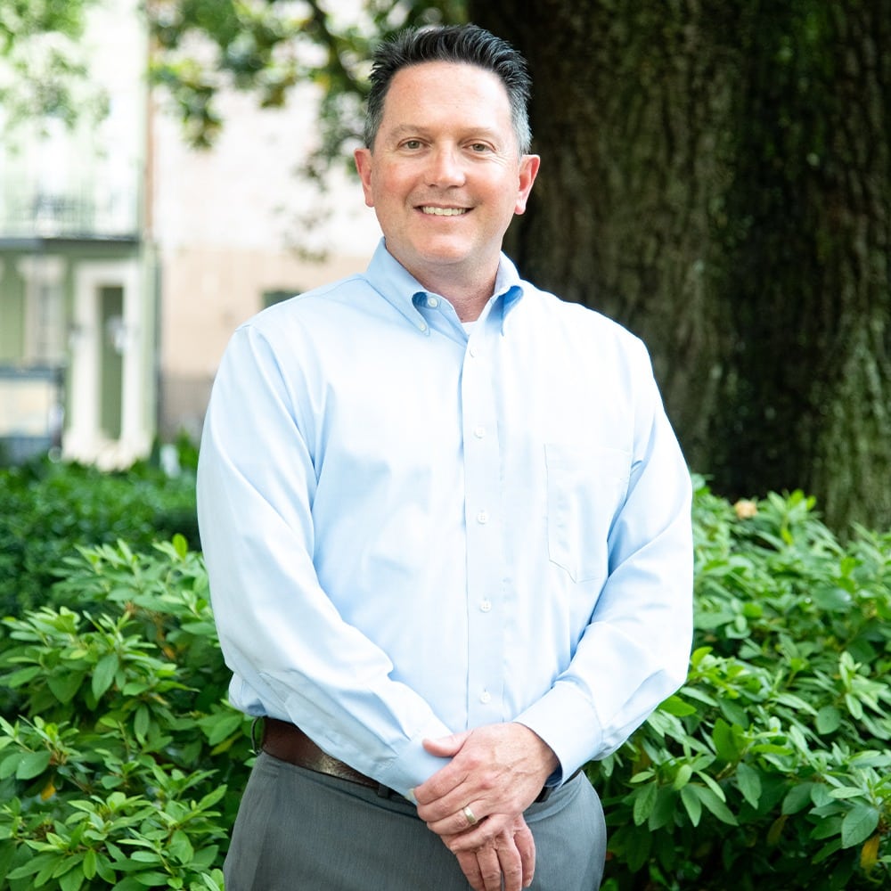 A leader in a blue shirt standing in front of bushes.