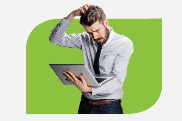 ransomeware1 A man holding a laptop and looking stressed, with his head in his hands.
