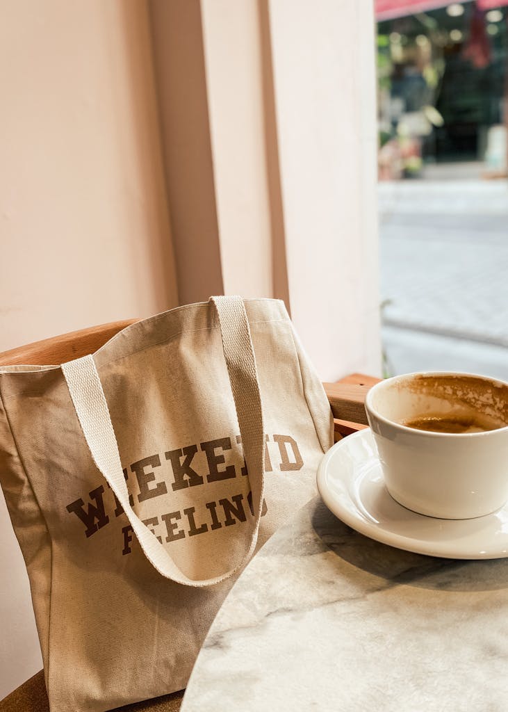Beige tote bag and coffee cup on a café table, perfect weekend vibe.