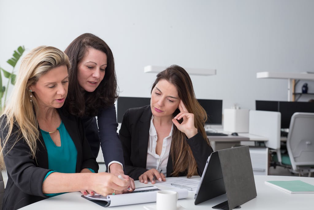 Three businesswomen collaborate on documents in a modern office setting.