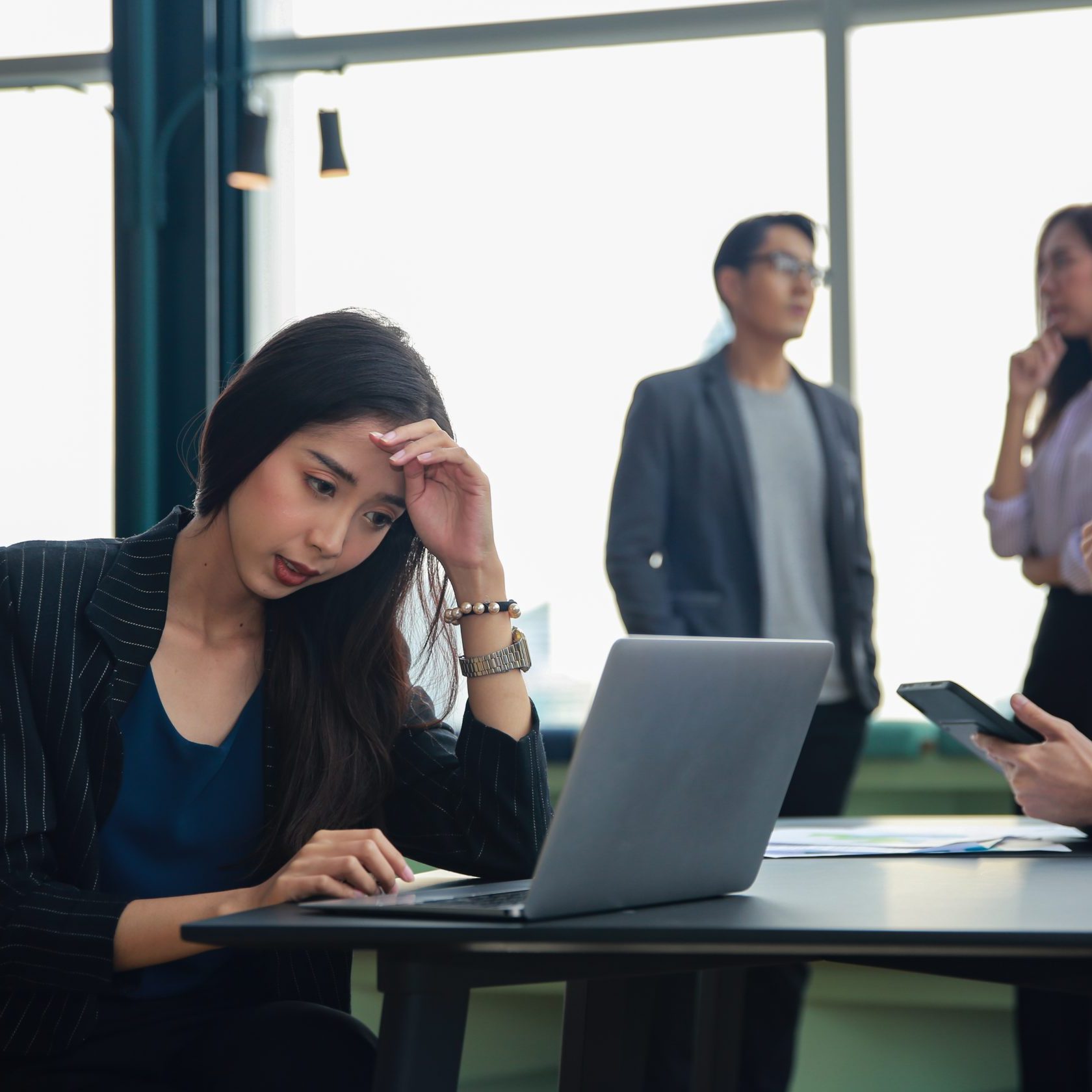A group of asian business people sitting around a table with laptops discussing a case study.